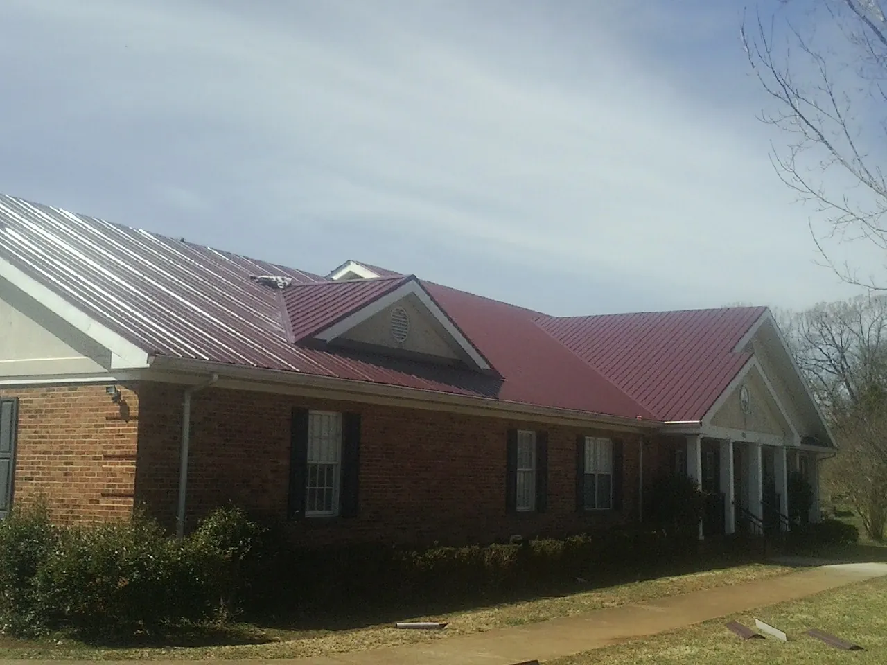 Red metal roof with gabled entries on a long brick building, from a Hail Damage Roof Repair job in Pullman